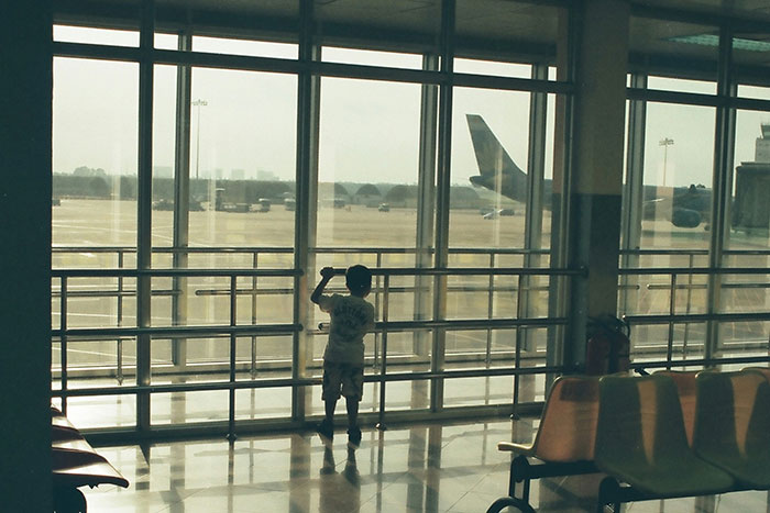 Child watching planes through airport window, capturing the normality of air travel in 2025.