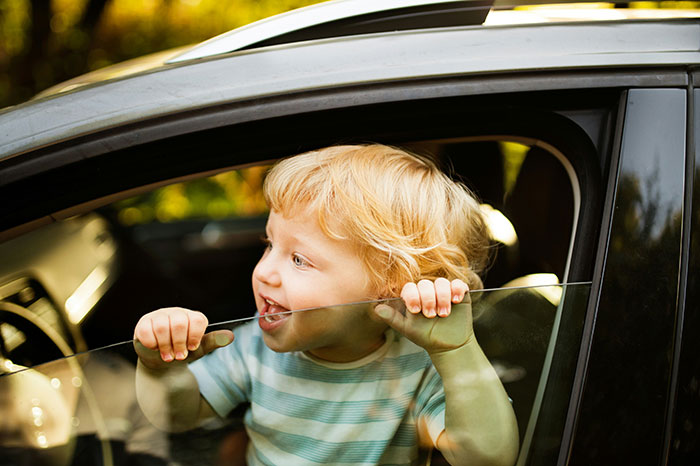 Toddler enjoying a car ride, leaning out the window, capturing a moment from simpler times remembered as normal.