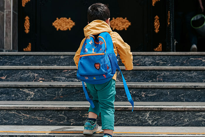 Child climbing stairs with a colorful backpack, evoking nostalgic memories and changes by 2025.