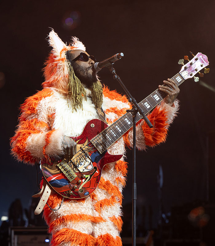 Celebrity in orange and white fur costume playing guitar at Coachella 2025, weekend two.