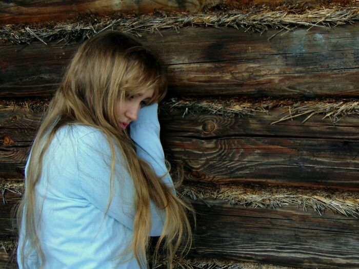 Person in blue shirt leaning against a wooden wall, conveying a sense of something traumatizing.
