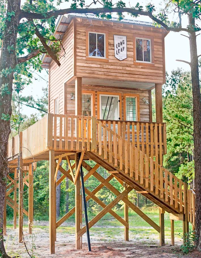 Wooden tiny home elevated on stilts with a large deck surrounded by trees, showcasing unique tiny homes off the grid.