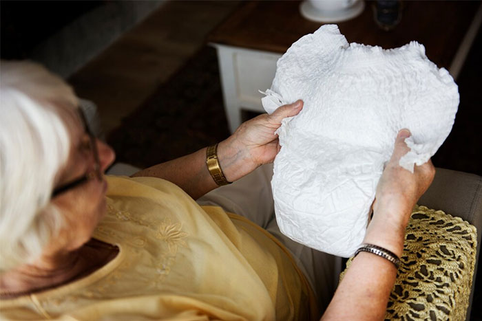 Elderly person in a yellow shirt examining a large white diaper, illustrating a fun fact.
