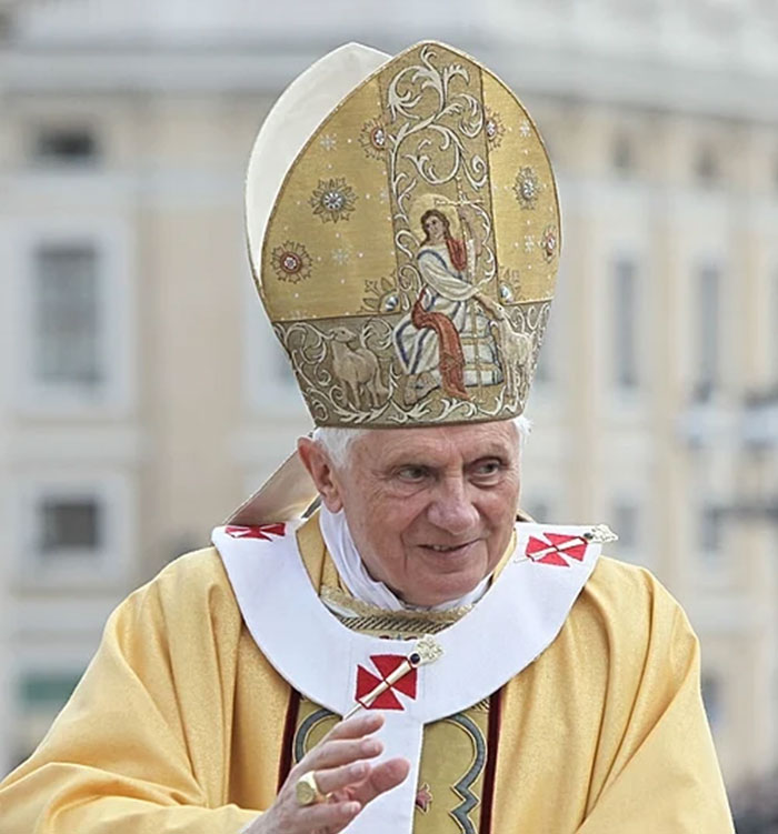 A religious leader wearing an ornate mitre and robe, sharing a moment during a public event.