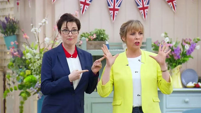 Two women stand in a decorated room with British flags, engaging in a lively discussion.