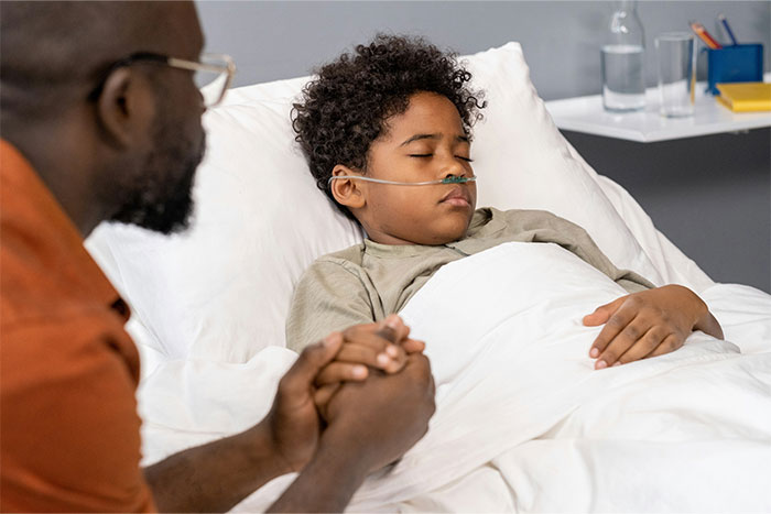 Child resting in hospital bed with an adult holding their hand, creating a supportive atmosphere.