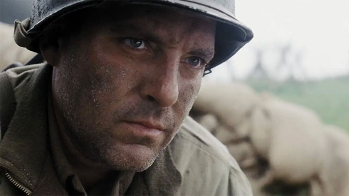 A soldier in a dirt-smeared uniform and helmet, focusing intensely, with a blurred background of sandbags. Fun facts context.
