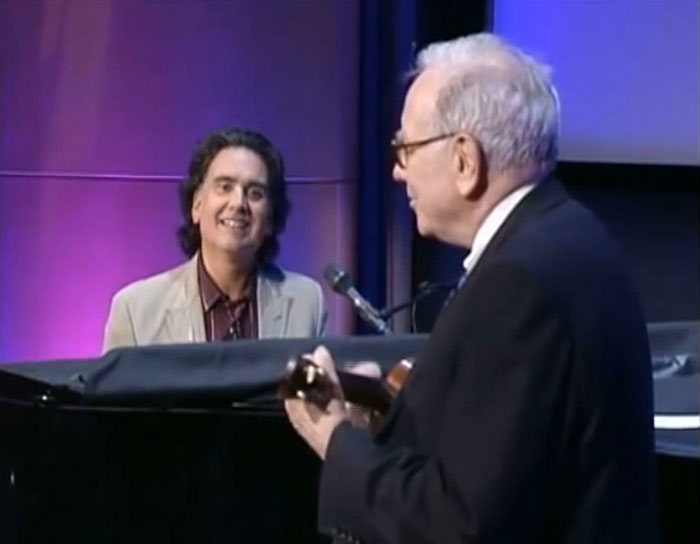 A man playing ukulele while another smiles at the piano, engaging with fun facts.