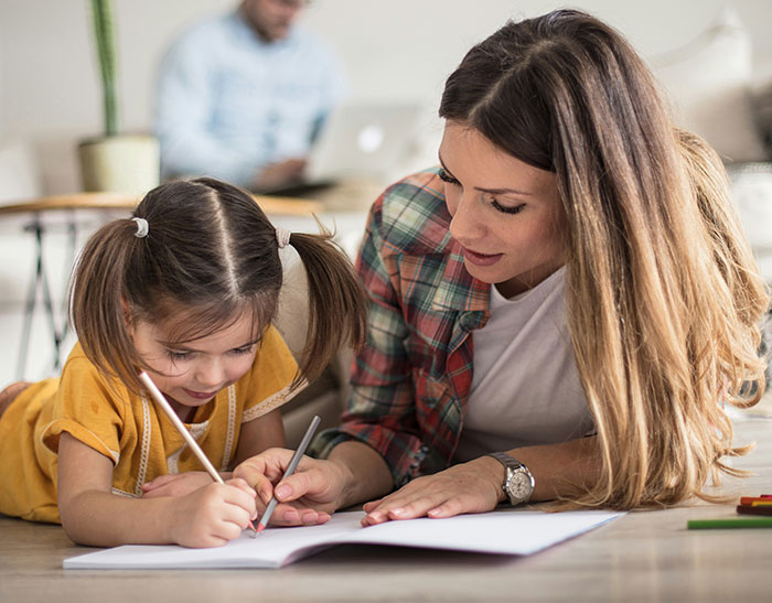 A mother helps her daughter with homework at home, focusing on learning and support.