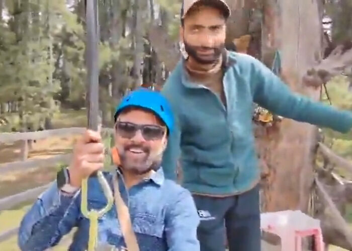 Tourist smiling while zip-lining with guide nearby in forested area during tragic event that took 26 lives.