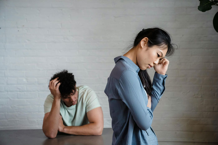 Woman turns away, distressed, while a man sits at a table with head in hands, illustrating a tense family trip discussion.
