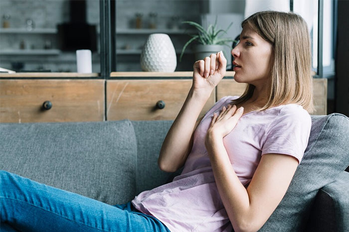 A woman sits on a couch, coughing into her hand, reflecting on life-saving facts.