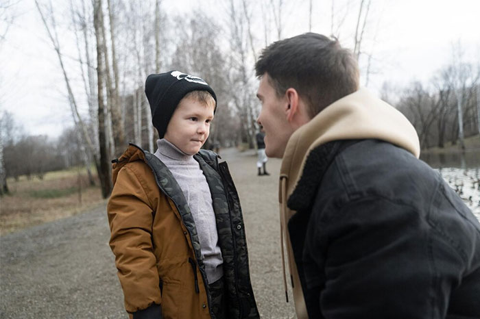 A man in a jacket crouches to talk to a child in the park, sharing life-saving advice.