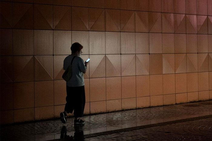 Person walking alone at night, looking at a phone, highlighting life-saving awareness in dimly lit environments.