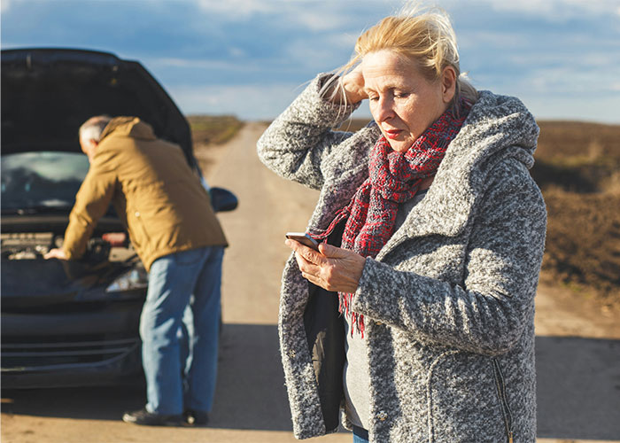Woman in winter clothing using her phone for help while man checks car engine, illustrating life-saving facts.