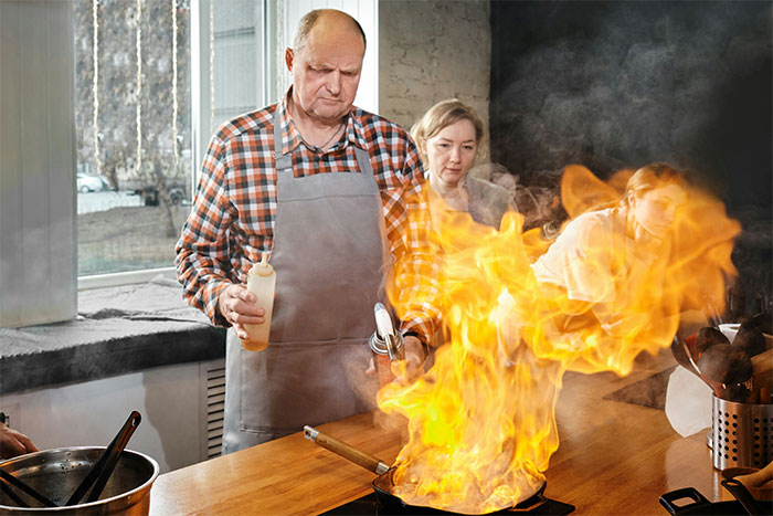 A man in an apron handling a kitchen fire, demonstrating a life-saving cooking tip.