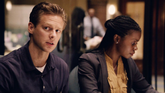 Two people in a serious discussion at a conference table, reflecting high-quality TV show scenes.