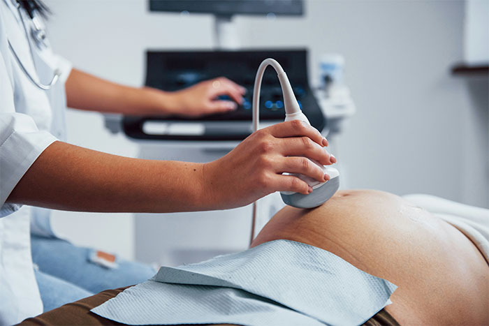 Ultrasound being performed on pregnant woman’s belly by a medical professional.