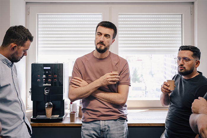 Men having coffee and chatting in a casual setting, standing by a coffee machine.