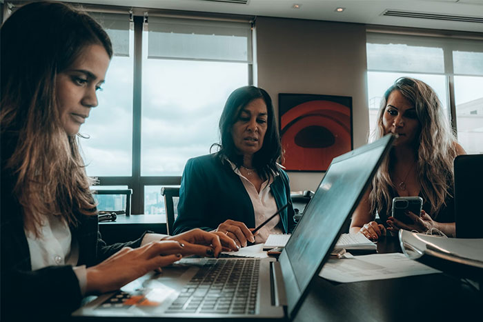 Women in a meeting room, collaborating on laptops and documents, with a focus on inappropriate things said to pregnant women.