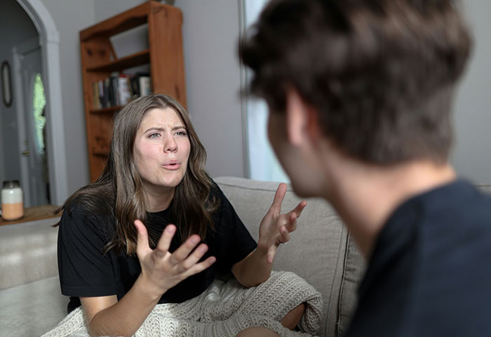Pregnant woman looking frustrated during conversation on a couch, likely reacting to an inappropriate remark.