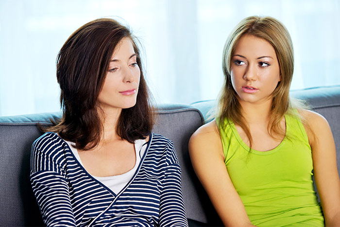 Two women sitting on a couch exchanging awkward looks, discussing wildly inappropriate comments about pregnancy.