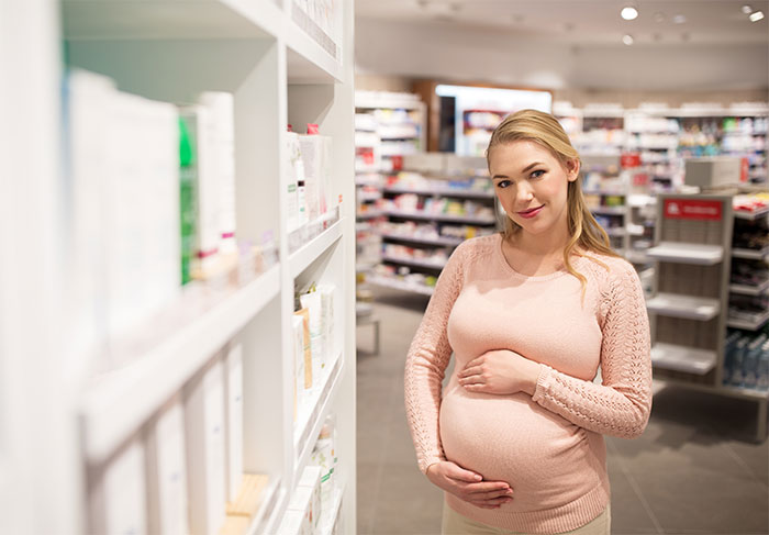 Pregnant woman in a pharmacy, gently holding her belly, surrounded by shelves of products.