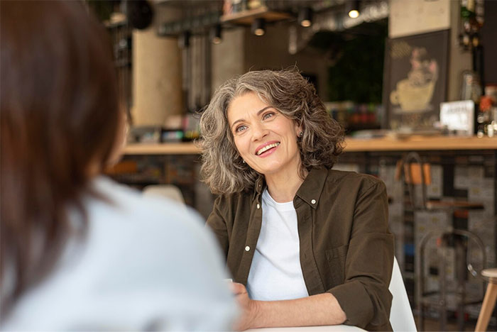 Smiling woman in a casual cafe setting, engaging in a conversation with a pregnant woman.