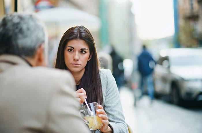 Woman listening intently during an outdoor conversation, holding a beverage, reflecting on comments about pregnancy.