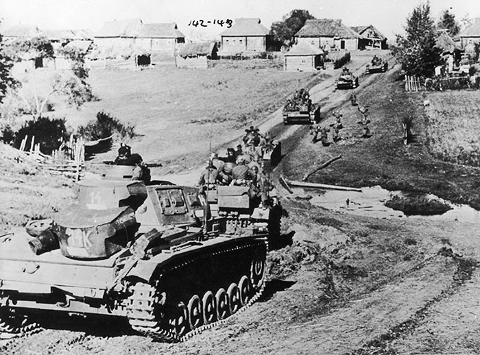 Historical tanks moving through a rural village road.