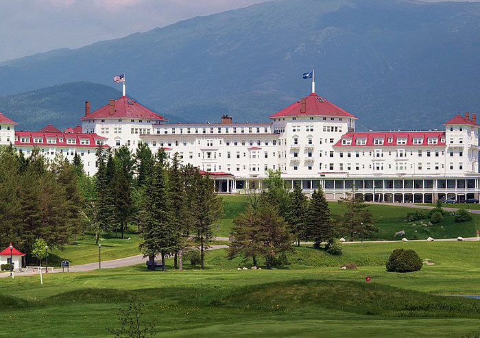 Historic grand hotel with red roofs and flags, surrounded by trees and mountains, showcasing moments in history importance.