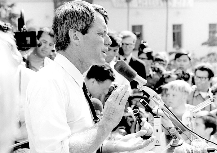 Black and white photo of a man speaking passionately into a microphone during a significant historical moment.