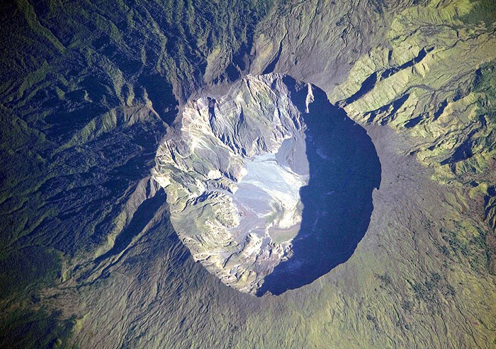 Aerial view of a volcanic crater surrounded by rugged terrain, highlighting a moment in history with geological importance.