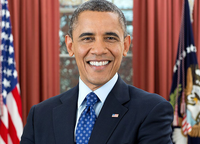 Portrait of a smiling man in a suit with flags in the background representing moments in history importance.