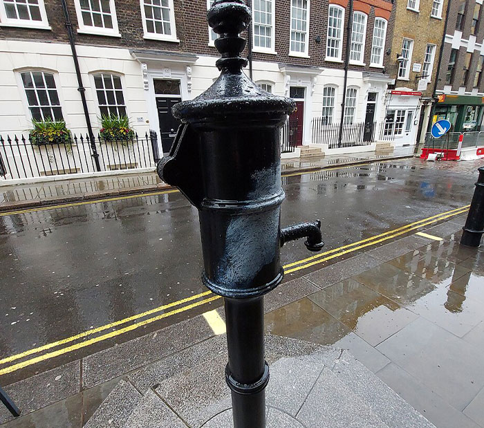 Historic black water pump on a wet street, representing moments in history people may not realize how important they were.