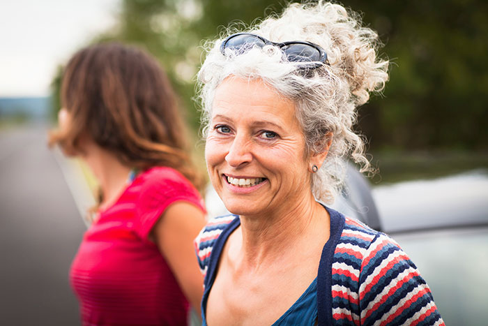 Older woman smiling outdoors, embodying unique beauty hacks.