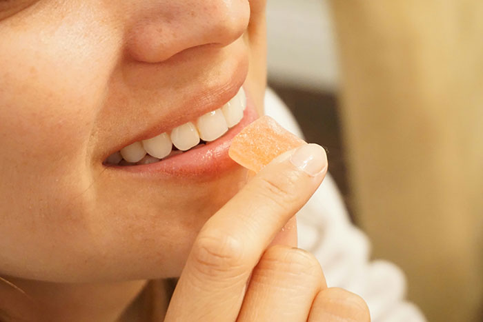 Person trying an unhinged beauty hack by holding a small orange item near their lips.