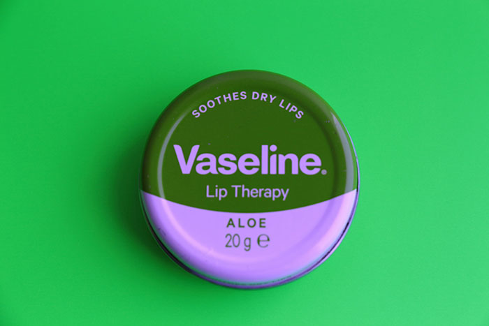Vaseline Lip Therapy Aloe tin on green background, highlighting beauty hacks for dry lips.