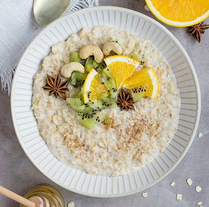 Bowl of oatmeal topped with kiwi, orange slices, cashews, and star anise.