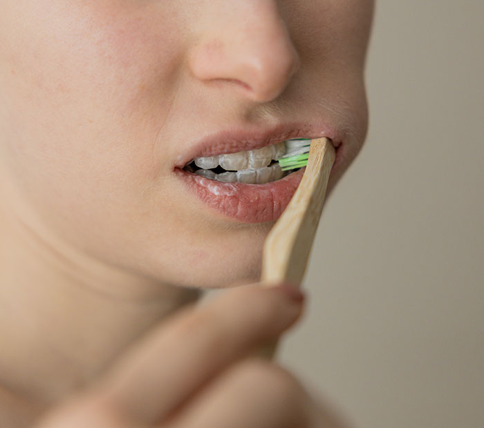 Person brushing teeth with a wooden toothbrush as a unique beauty hack.