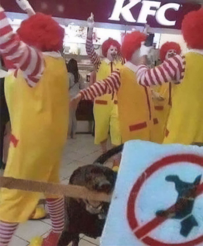 Cursed image of clowns at a KFC, while a dog holds a no-dog sign in its mouth.