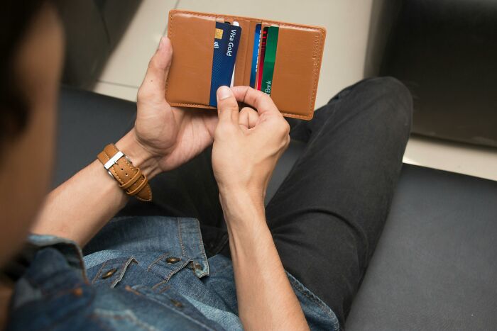Man holding a brown wallet with credit cards, illustrating frustrations from things exes did that still make blood boil