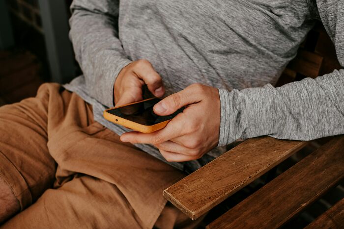 Person in casual clothes sitting on wooden chair, holding a smartphone, reflecting on things exes did that anger still.