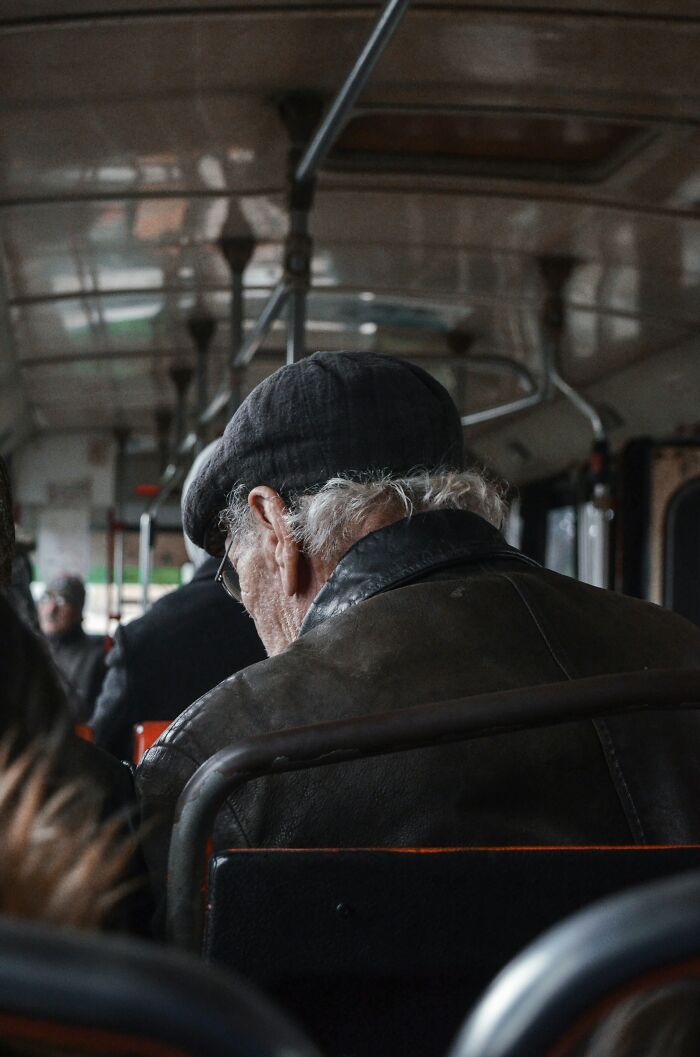 Elderly man wearing a cap and leather jacket sitting quietly on a bus, reflecting on things exes did that still make blood boil.