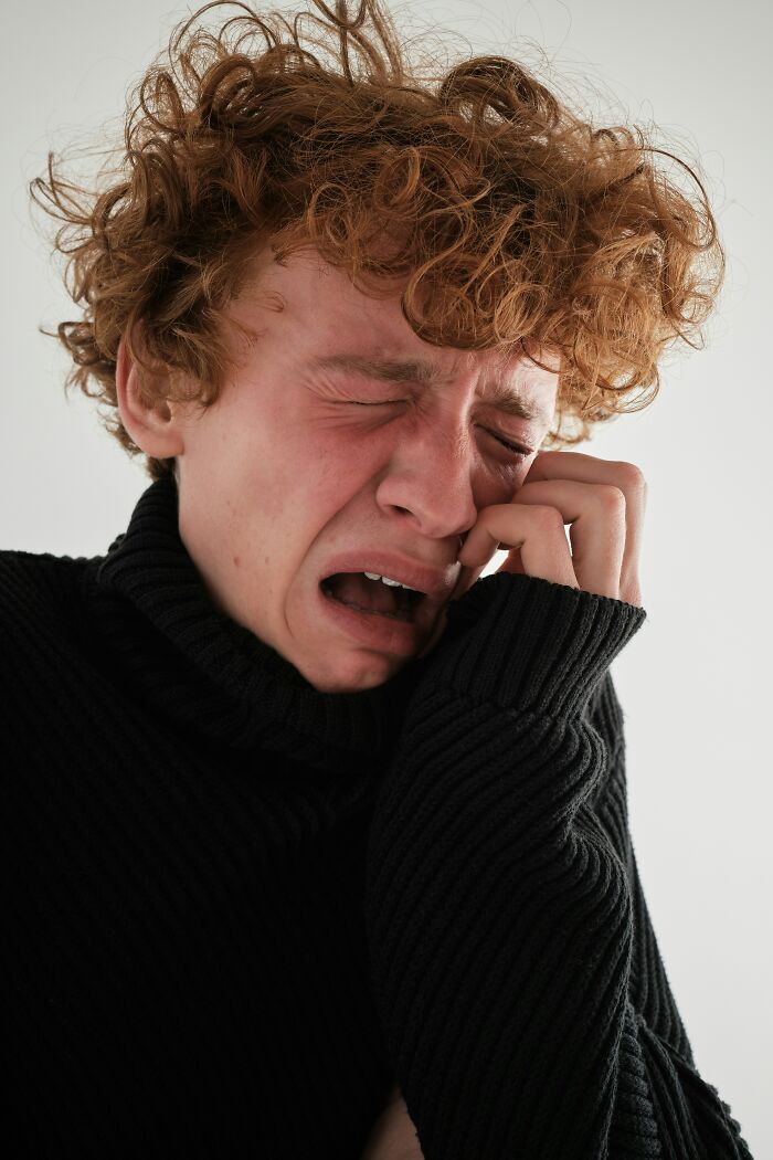 Young person with curly hair crying intensely, expressing distress and anger related to people's exes actions in black sweater.