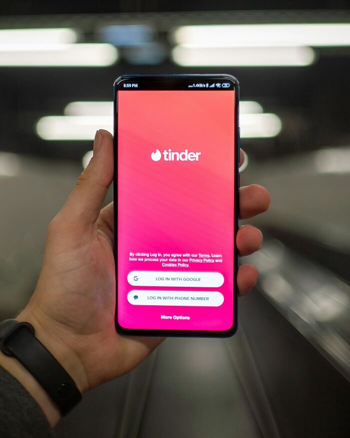 Hand holding smartphone displaying Tinder app login screen, related to exes and dating frustrations.