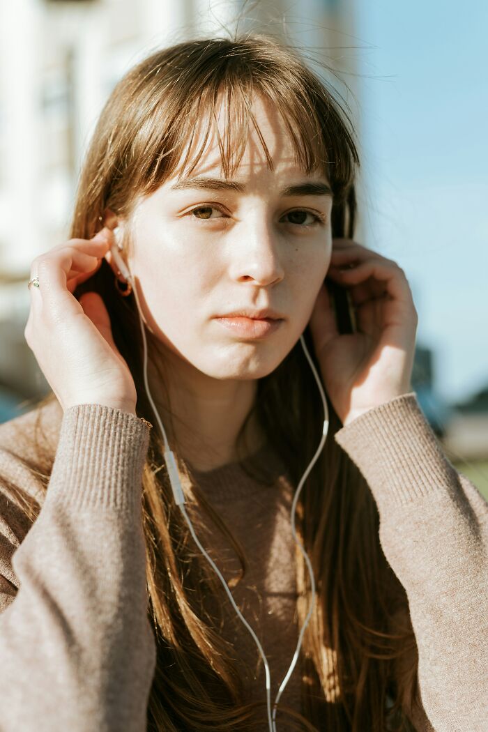 Young woman with earphones outdoors, appearing thoughtful, reflecting emotions linked to people's exes memories.