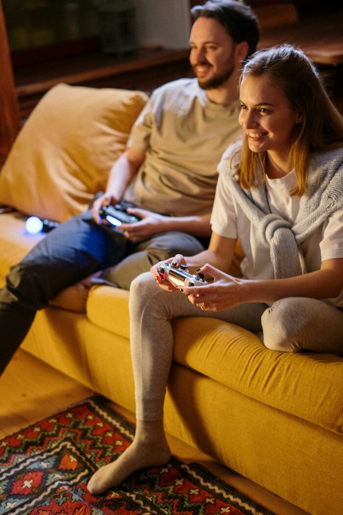 Young couple playing video games together on a yellow couch, highlighting moments from people's exes that still make blood boil.