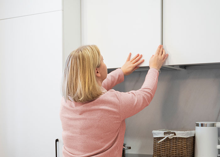 Woman in a kitchen reaching for a cabinet, illustrating household marriage hack.