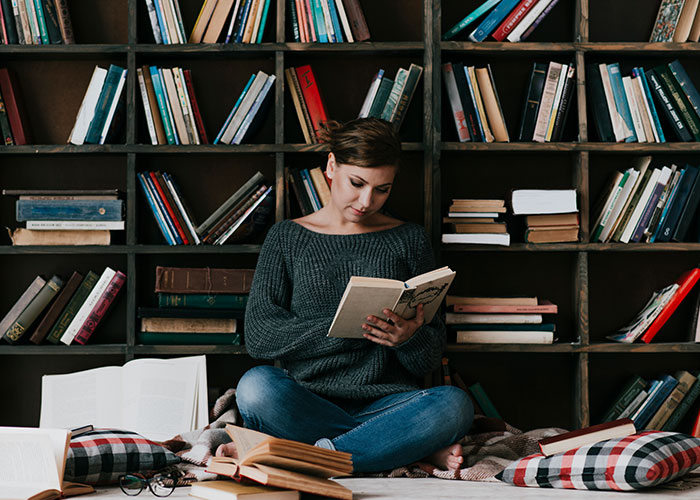 Woman sitting on the floor, reading a book, surrounded by bookshelves, reflecting on wild marriage hacks.